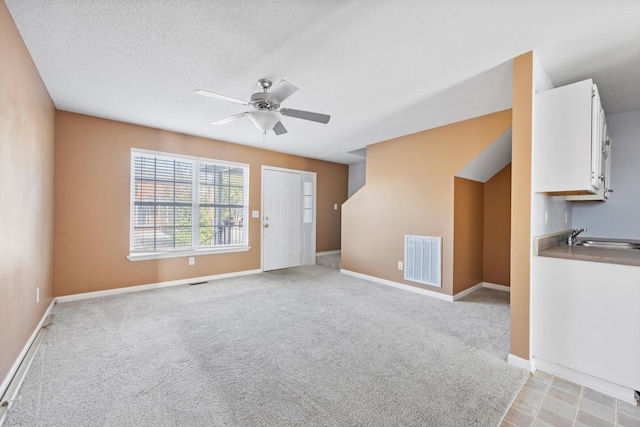 unfurnished living room featuring ceiling fan, sink, light colored carpet, and a textured ceiling