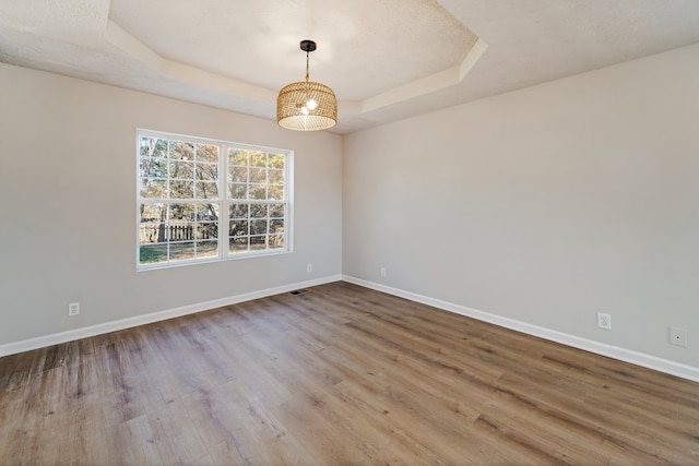 empty room with a raised ceiling, a textured ceiling, and hardwood / wood-style flooring