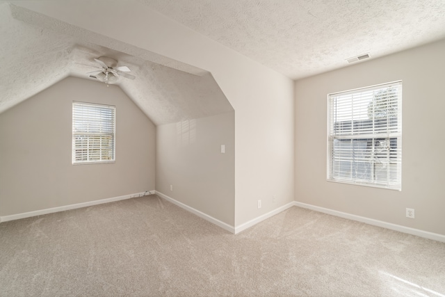 additional living space with lofted ceiling, ceiling fan, light colored carpet, and a textured ceiling