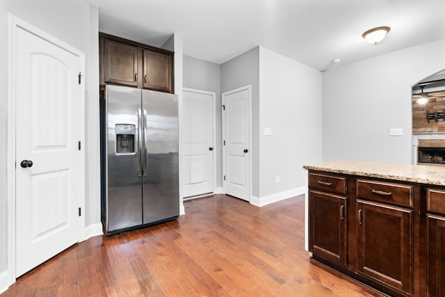 kitchen featuring dark hardwood / wood-style floors, stainless steel fridge, tasteful backsplash, light stone counters, and dark brown cabinetry