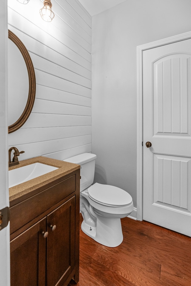 bathroom featuring hardwood / wood-style flooring, vanity, wood walls, and toilet