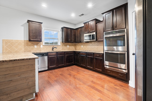 kitchen with decorative backsplash, appliances with stainless steel finishes, light wood-type flooring, light stone counters, and sink