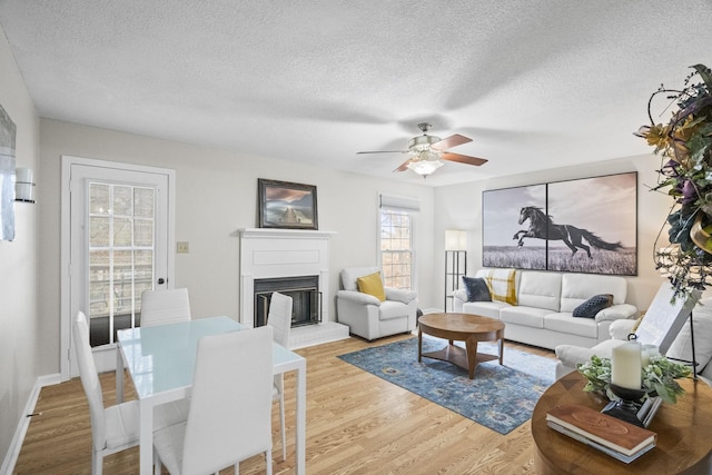 living room featuring a fireplace, light hardwood / wood-style floors, a textured ceiling, and ceiling fan