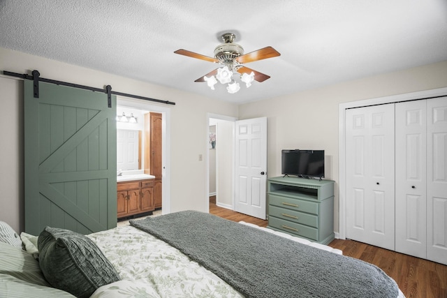 bedroom with ceiling fan, a barn door, dark wood-type flooring, and a closet