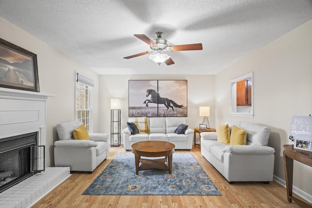 living room with a textured ceiling, light wood-type flooring, a brick fireplace, and ceiling fan