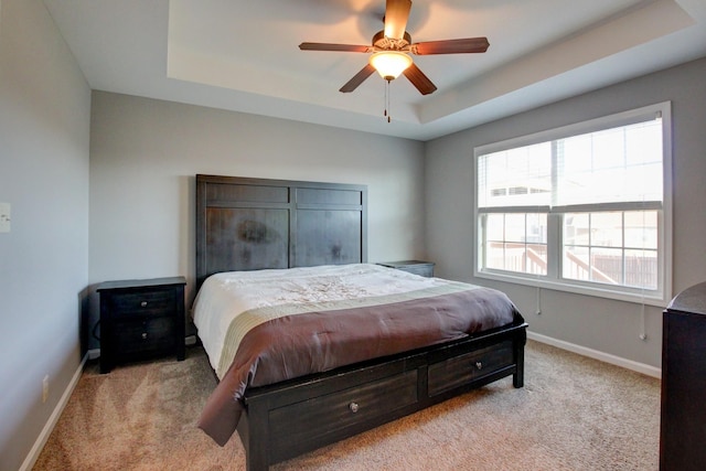 bedroom with ceiling fan, multiple windows, and a tray ceiling