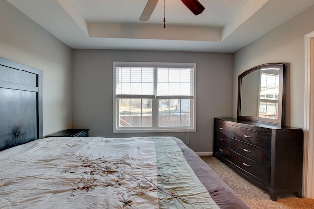 bedroom with light carpet, ceiling fan, a tray ceiling, and multiple windows