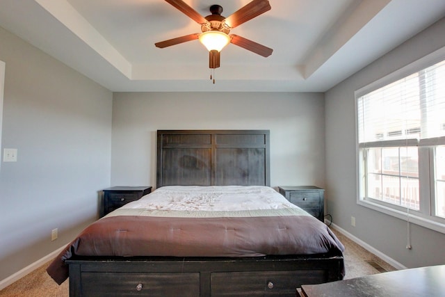 carpeted bedroom with ceiling fan, a tray ceiling, and multiple windows