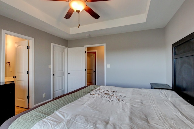 bedroom featuring ceiling fan, a tray ceiling, and ensuite bath