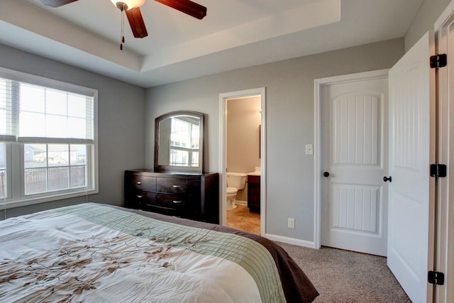 carpeted bedroom featuring a raised ceiling, ensuite bath, ceiling fan, and multiple windows