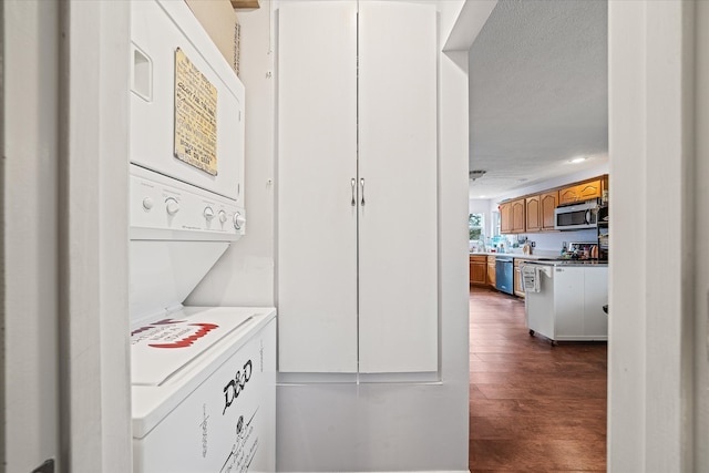 laundry room with a textured ceiling, dark hardwood / wood-style flooring, and stacked washer and clothes dryer