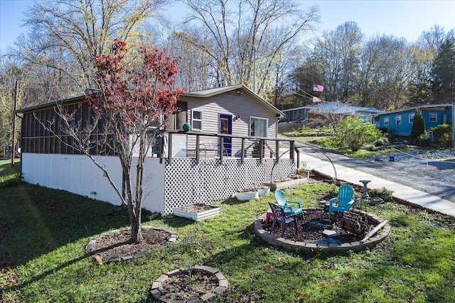 view of side of home featuring a sunroom, a yard, a fire pit, and a deck