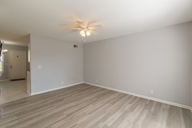 spare room with ceiling fan with notable chandelier and light hardwood / wood-style floors