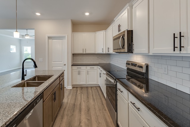 kitchen with white cabinets, hanging light fixtures, sink, dark stone countertops, and appliances with stainless steel finishes