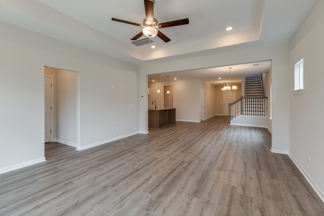 unfurnished living room with a raised ceiling, light hardwood / wood-style flooring, ceiling fan with notable chandelier, and sink