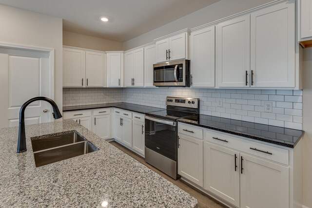 kitchen with backsplash, white cabinets, sink, light stone counters, and stainless steel appliances