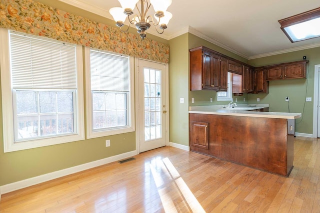 kitchen featuring decorative light fixtures, kitchen peninsula, ornamental molding, and an inviting chandelier