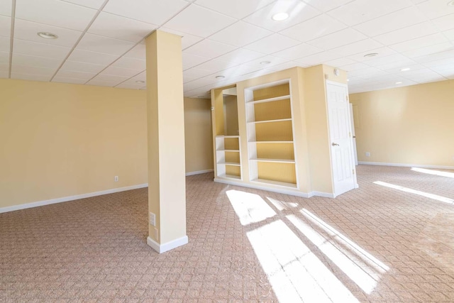 basement featuring carpet, built in features, and a drop ceiling