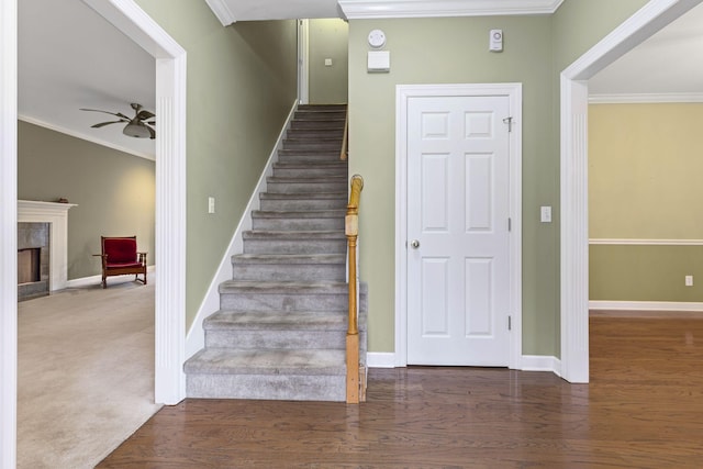 stairway with hardwood / wood-style floors, a fireplace, ornamental molding, and ceiling fan