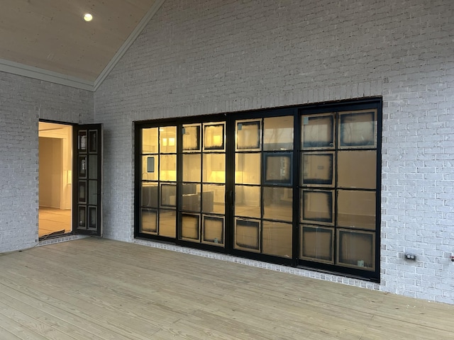 empty room with lofted ceiling, crown molding, brick wall, and light wood-type flooring