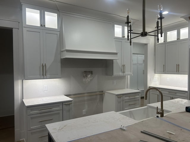 kitchen with sink, gray cabinetry, light stone counters, tasteful backsplash, and custom range hood