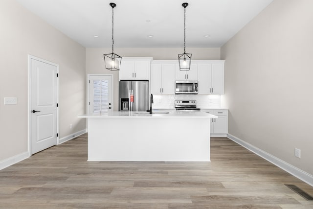 kitchen with appliances with stainless steel finishes, a center island with sink, and white cabinetry