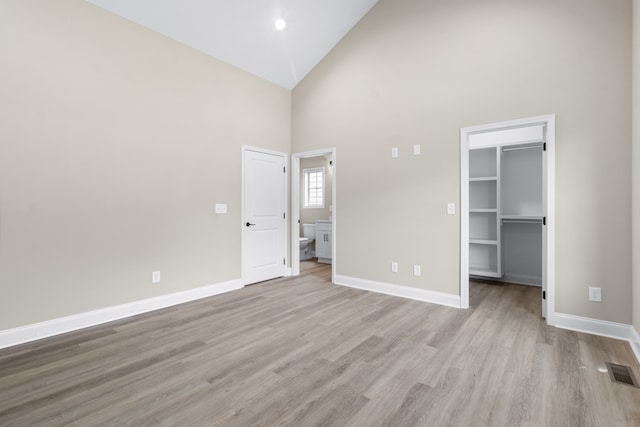 unfurnished bedroom with a closet, a walk in closet, high vaulted ceiling, and light hardwood / wood-style flooring