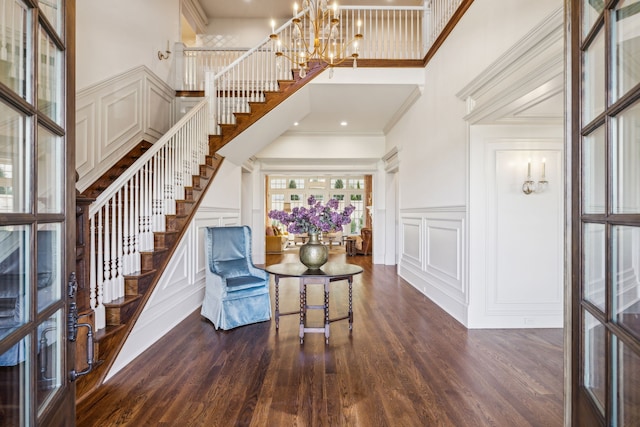 foyer entrance with french doors, dark wood-type flooring, a high ceiling, an inviting chandelier, and crown molding