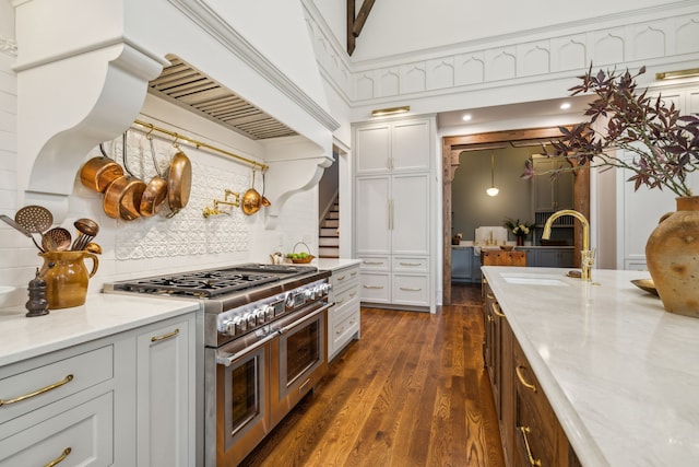 kitchen with sink, light stone counters, dark hardwood / wood-style floors, pendant lighting, and range with two ovens