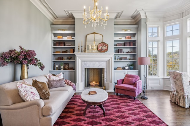 living room featuring built in shelves, crown molding, wood-type flooring, a premium fireplace, and a chandelier