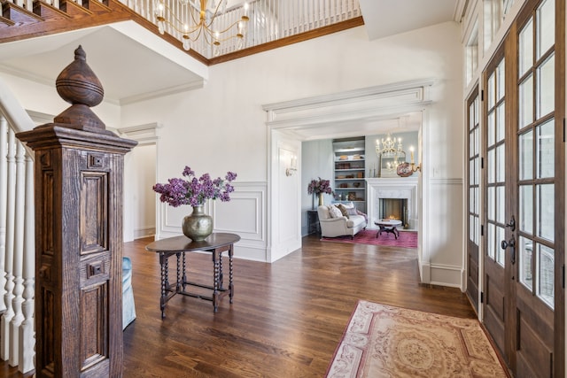 entrance foyer featuring french doors, dark wood-type flooring, a high ceiling, a chandelier, and ornamental molding