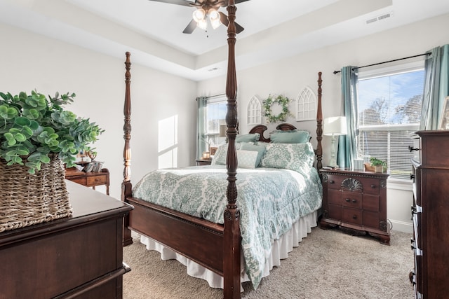 bedroom with ceiling fan, light colored carpet, a tray ceiling, and multiple windows