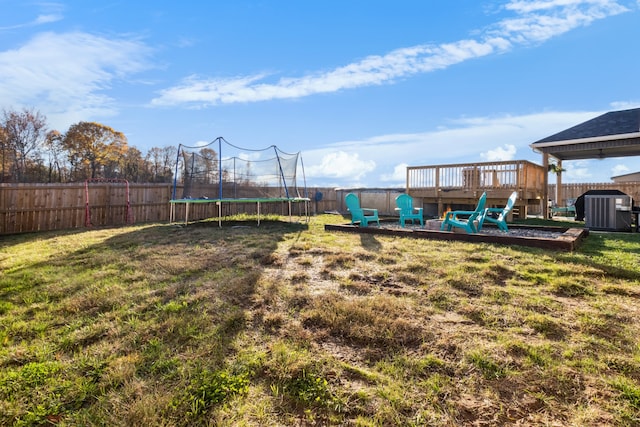 view of yard featuring a trampoline, central AC unit, and a wooden deck