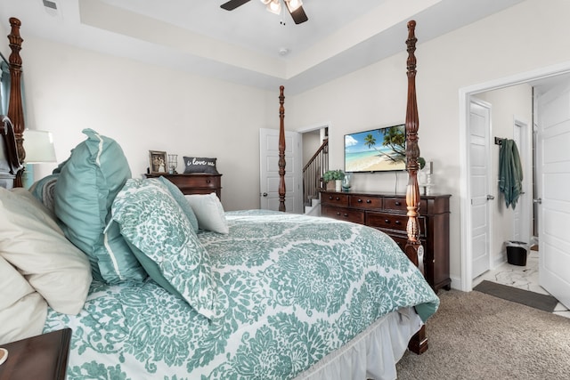 bedroom featuring ceiling fan, ensuite bath, light carpet, and a tray ceiling