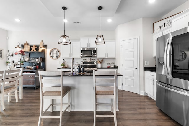 kitchen with appliances with stainless steel finishes, decorative light fixtures, white cabinetry, and dark wood-type flooring