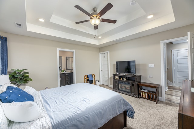 carpeted bedroom with a tray ceiling, ensuite bath, and ceiling fan