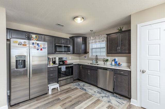 kitchen with stainless steel appliances, hanging light fixtures, light hardwood / wood-style floors, and sink