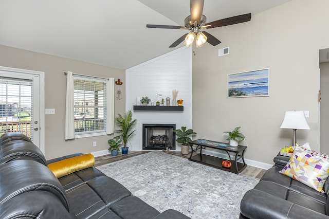 living room with hardwood / wood-style floors, ceiling fan, a large fireplace, and vaulted ceiling