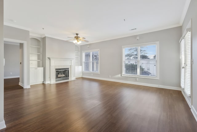 unfurnished living room with a tile fireplace, dark hardwood / wood-style floors, ceiling fan, built in features, and ornamental molding