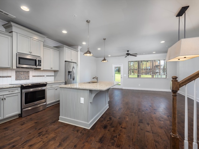 kitchen featuring light stone countertops, sink, stainless steel appliances, an island with sink, and decorative light fixtures