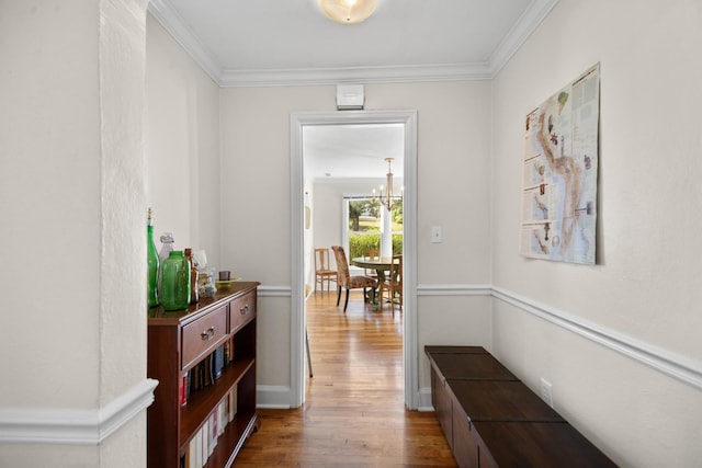 hall with wood-type flooring, an inviting chandelier, and ornamental molding