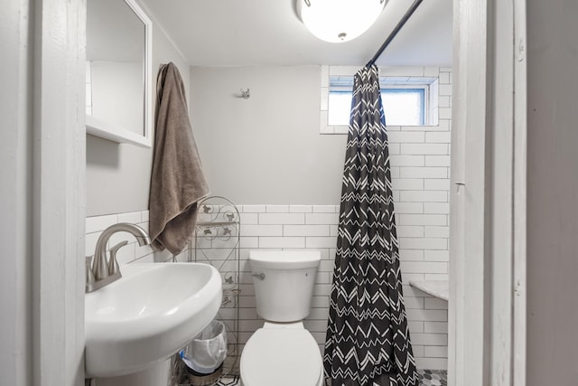 bathroom featuring toilet, tile walls, and sink