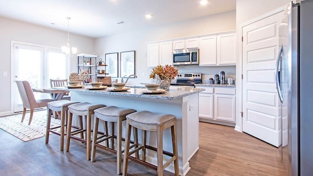 kitchen featuring appliances with stainless steel finishes, pendant lighting, a center island with sink, white cabinets, and light wood-type flooring