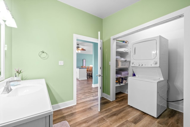 clothes washing area featuring hardwood / wood-style flooring, stacked washer and dryer, ceiling fan, and sink