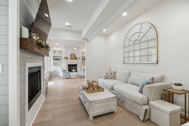 living room with built in shelves, light hardwood / wood-style floors, and ceiling fan