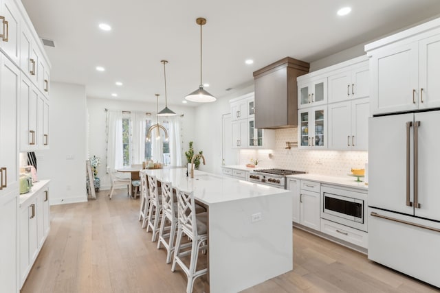 kitchen featuring a kitchen bar, light wood-type flooring, stainless steel appliances, a center island with sink, and white cabinets