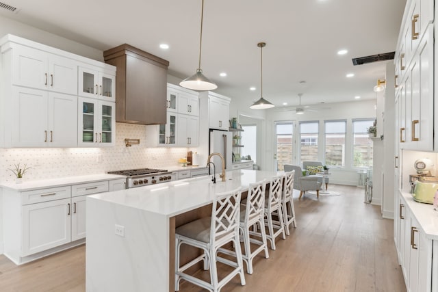 kitchen featuring a breakfast bar, a kitchen island with sink, ceiling fan, light hardwood / wood-style floors, and white cabinetry