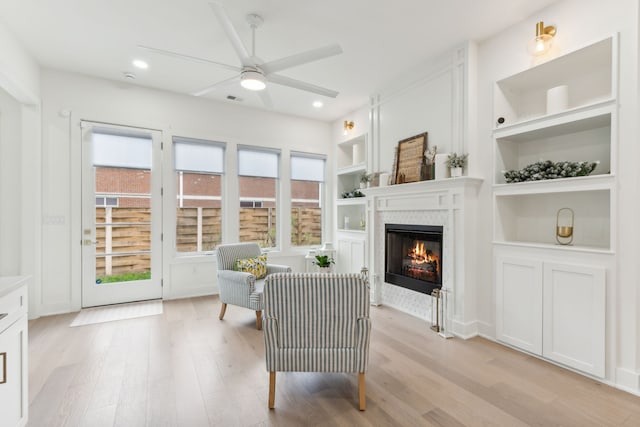 living area with built in shelves, light hardwood / wood-style floors, and ceiling fan