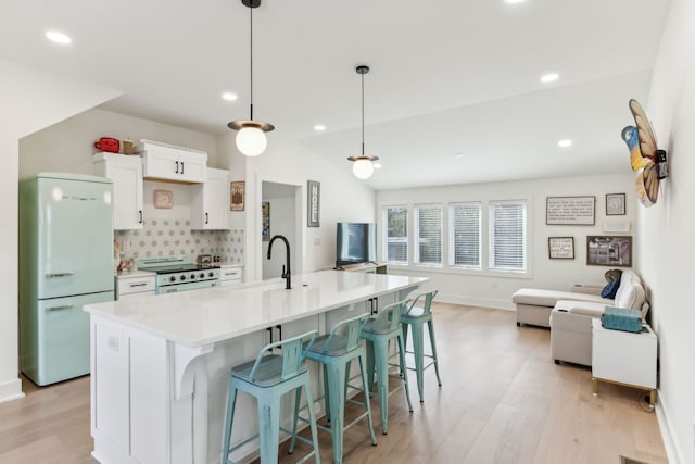 kitchen with white fridge, a spacious island, decorative light fixtures, white cabinets, and range