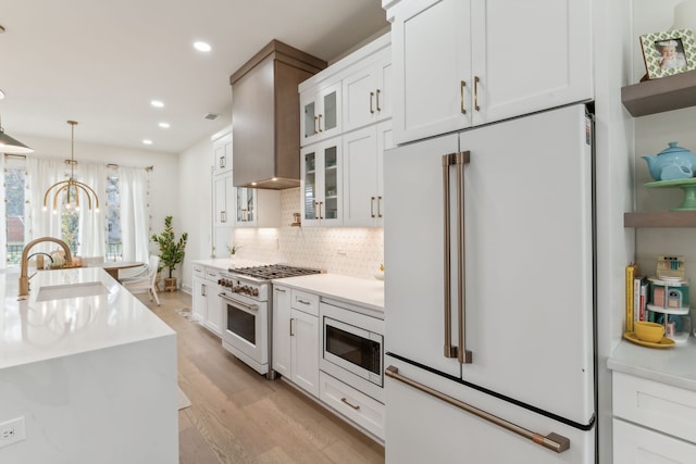 kitchen with high quality appliances, pendant lighting, white cabinets, and light hardwood / wood-style floors